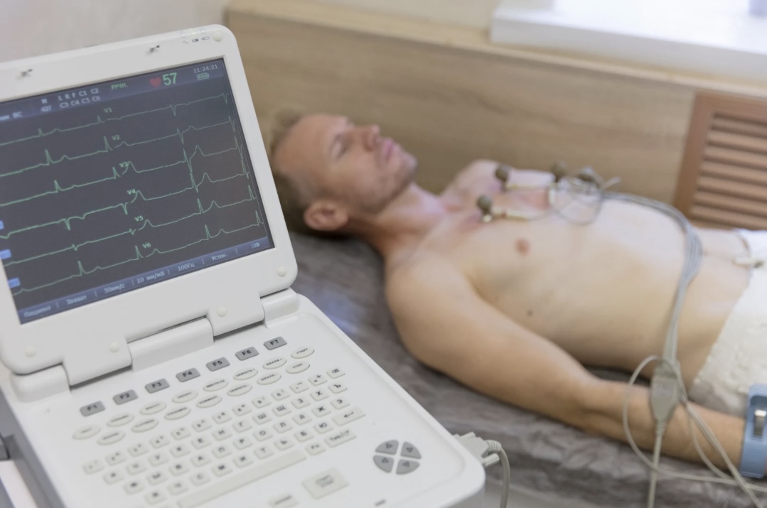 Patient liegt während einer EKG-Untersuchung, bei der Elektroden auf der Brust angebracht sind, zur Messung der elektrischen Aktivität des Herzens.