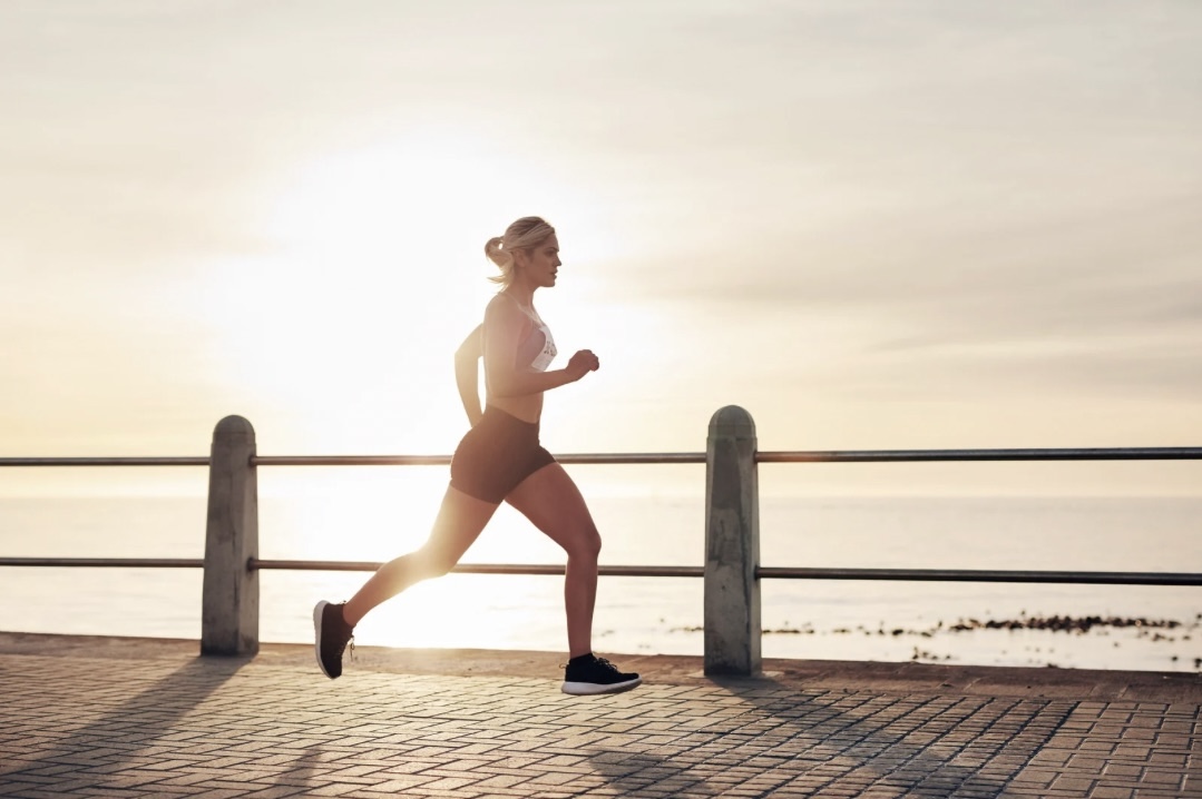 eine junge Frau beim Joggen am Meer im Sonnenaufgang